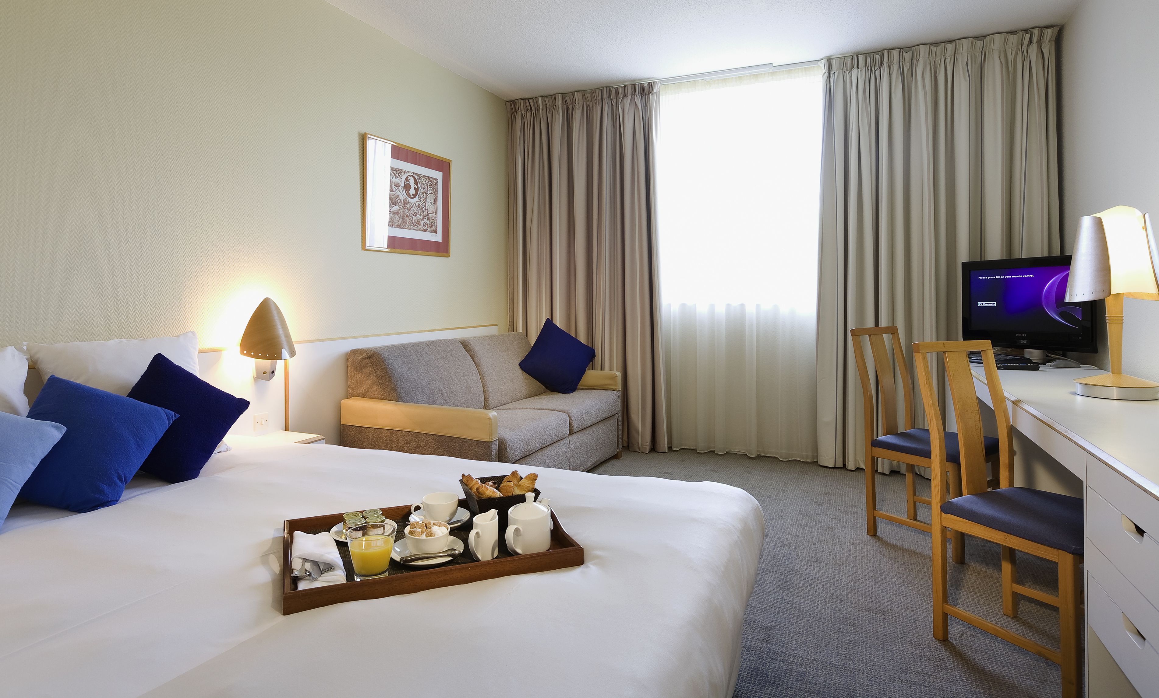 A hotel room with a bed, a desk, a chair, a TV, and a breakfast tray.