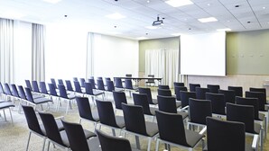 A conference room with rows of chairs, a projector screen, and a large window with curtains.