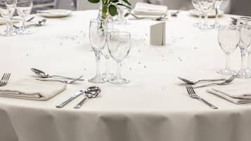 Una mesa redonda dispuesta para un evento formal, con cubertería de vidrio, servilletas dobladas y un jarrón con flores.