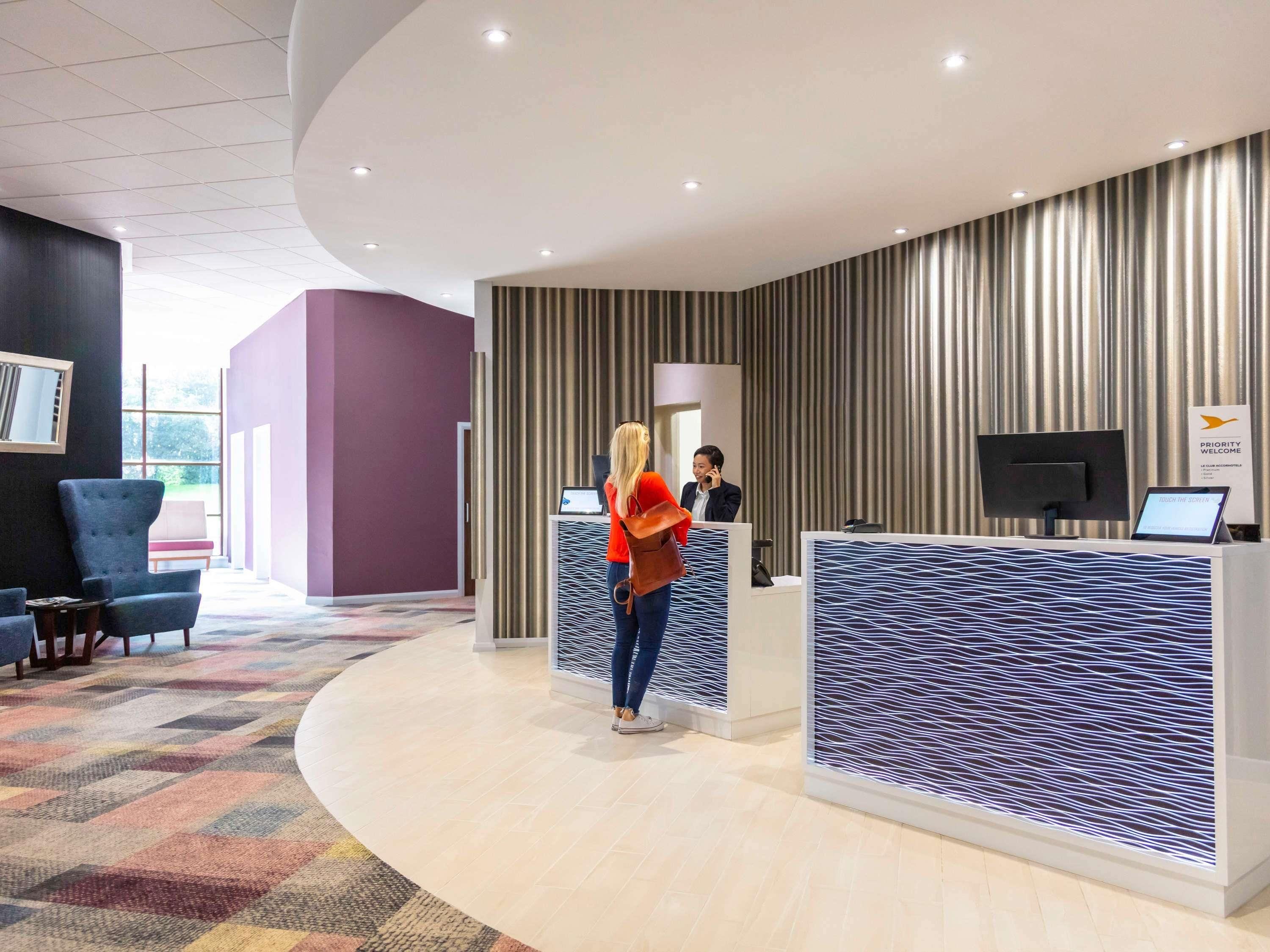 Un área de recepción moderna de hotel, con una alfombra curva, un mostrador de recepción y una pantalla grande.