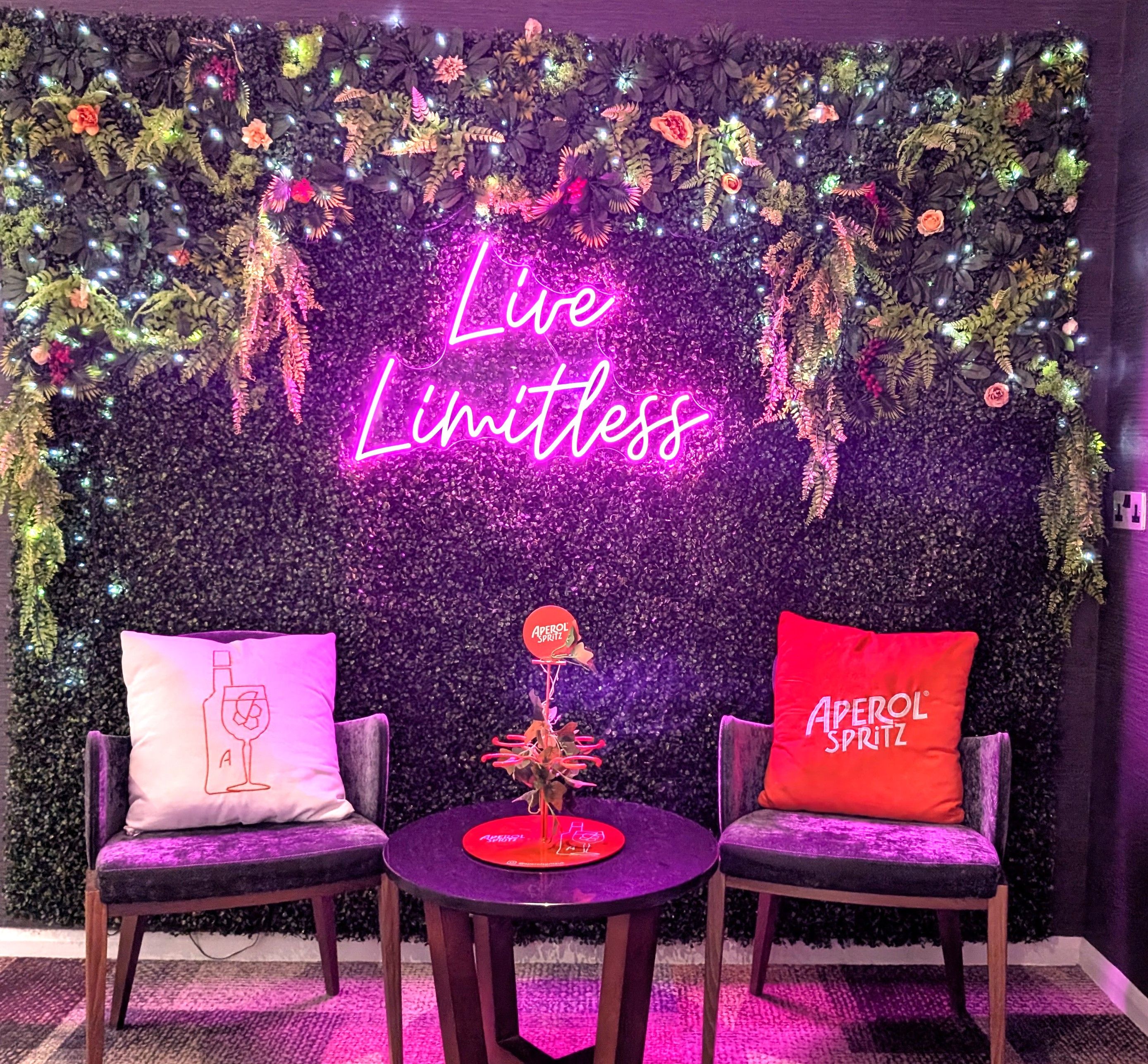 A room with a neon sign reading 'Live Limitless' and two chairs with pillows.