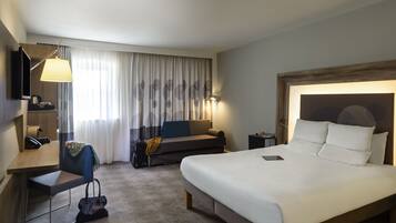 Une chambre d’hôtel avec un grand lit, un bureau avec une chaise, un canapé, une télévision et une lampe.