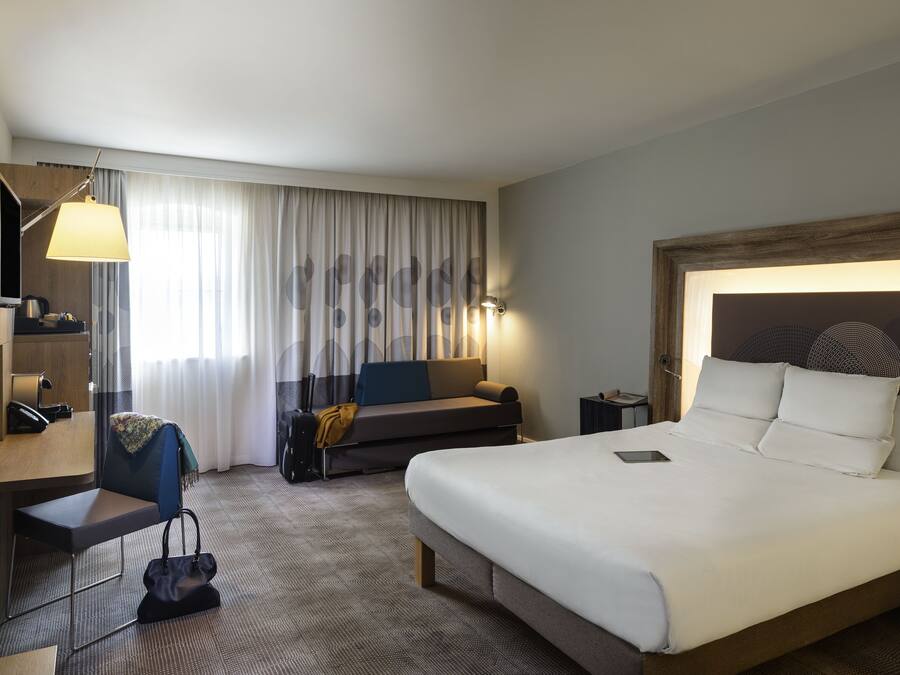 Une chambre d’hôtel avec un grand lit, un bureau avec une chaise, un canapé, une télévision et une lampe.