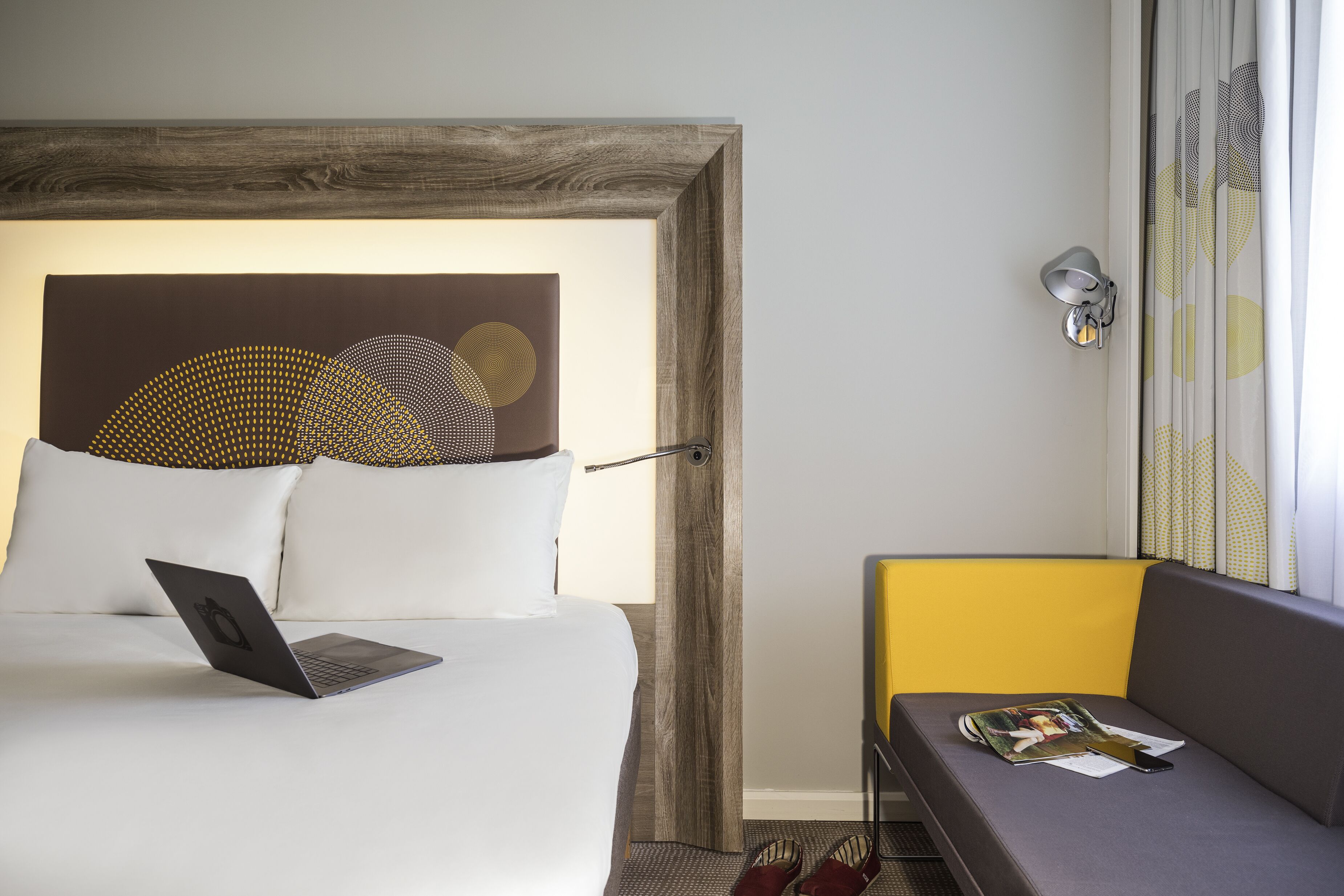 A hotel room with a bed, a laptop, a magazine, and a small table.