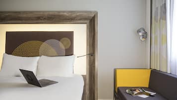A hotel room with a bed, a laptop, a magazine, and a small table.