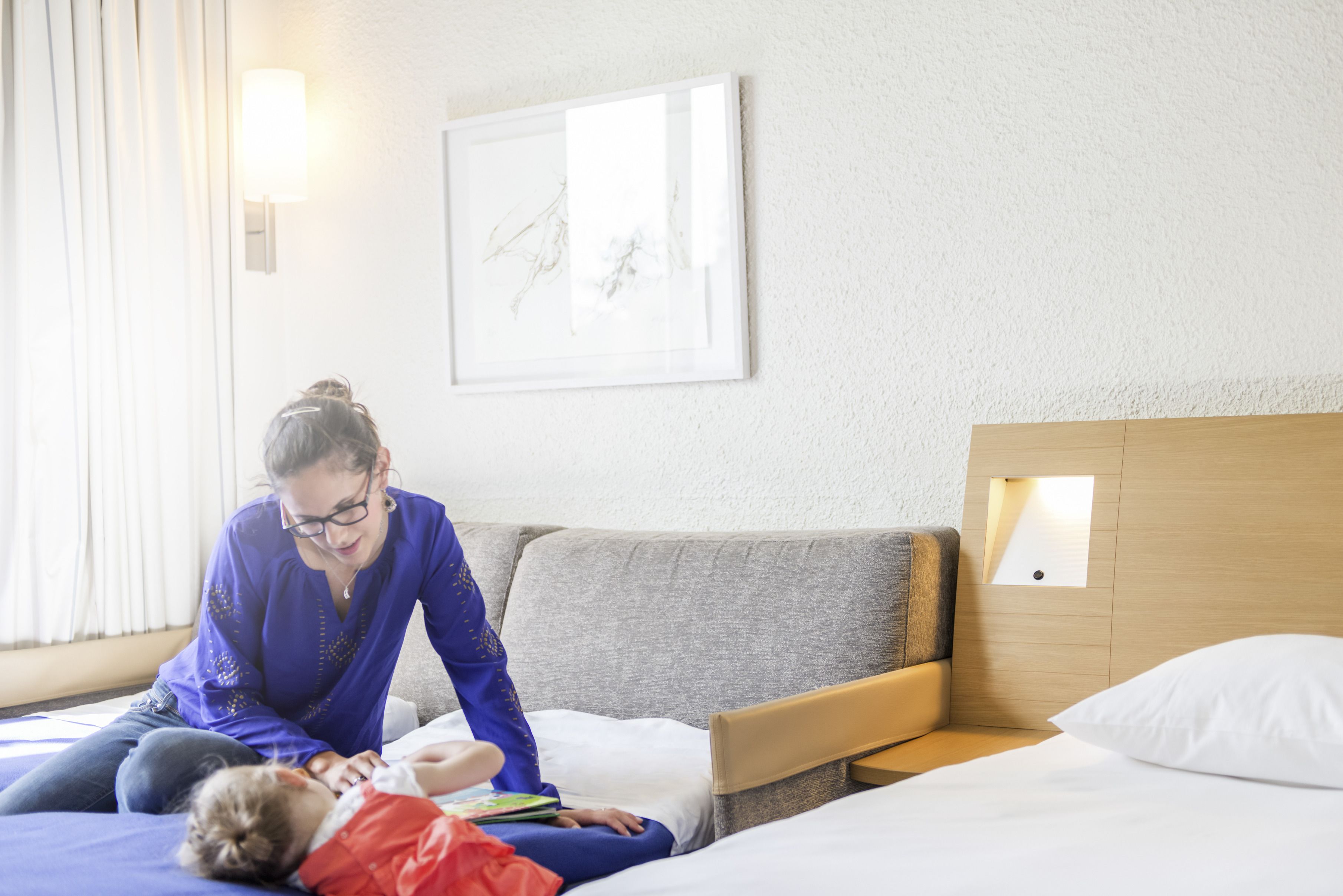 A hotel room with a bed, a bedside table, a wall-mounted light, and a framed picture on the wall.