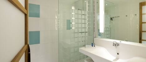 Un baño moderno con ducha de vidrio, lavamanos blanco y un espejo grande.