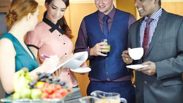 A group of people at a buffet with a variety of fruits and a pitcher of juice.
