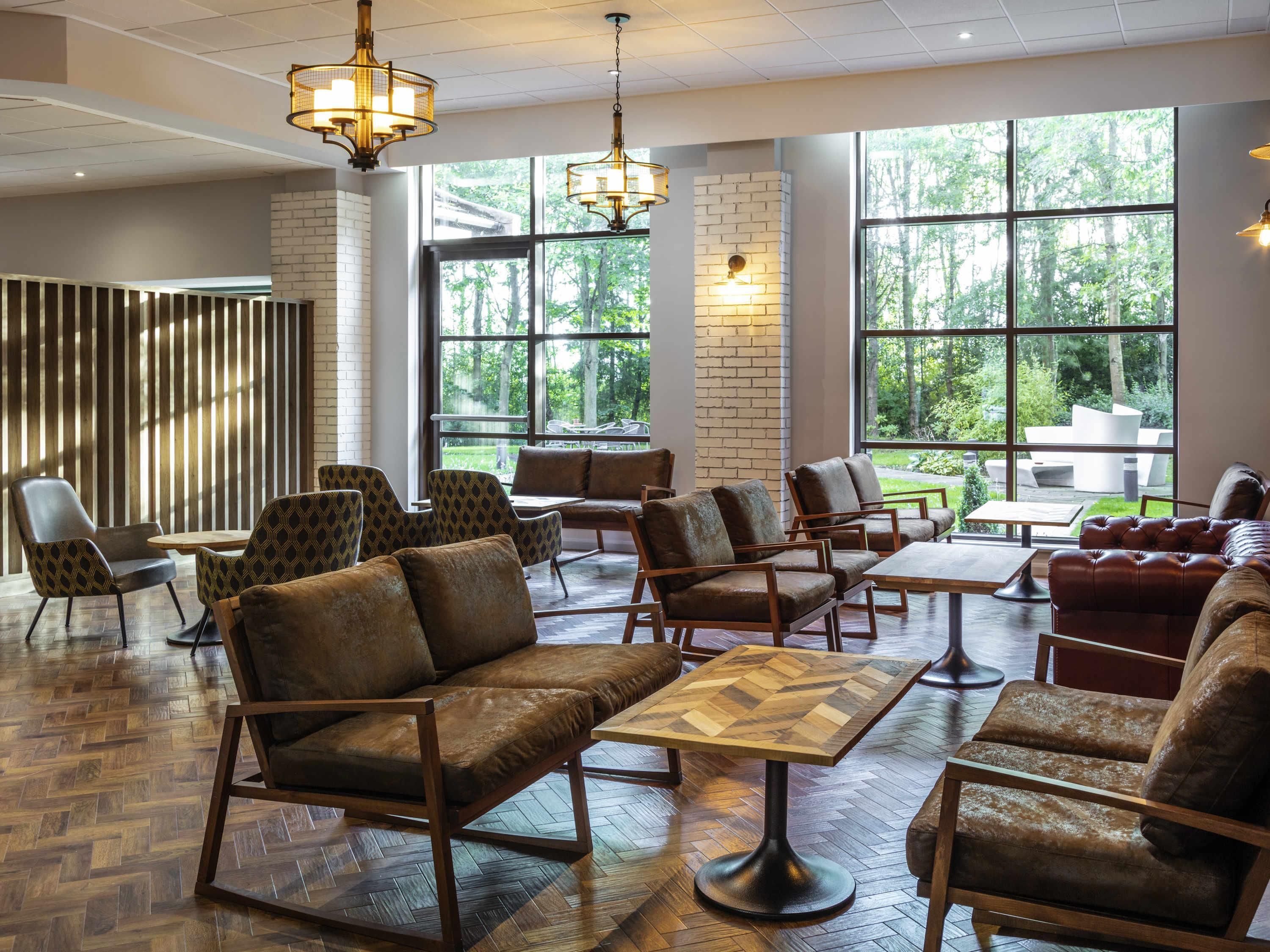 A spacious indoor area with multiple seating arrangements, large windows offering views of greenery, and modern lighting fixtures.