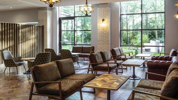 A spacious indoor area with multiple seating arrangements, large windows offering views of greenery, and modern lighting fixtures.