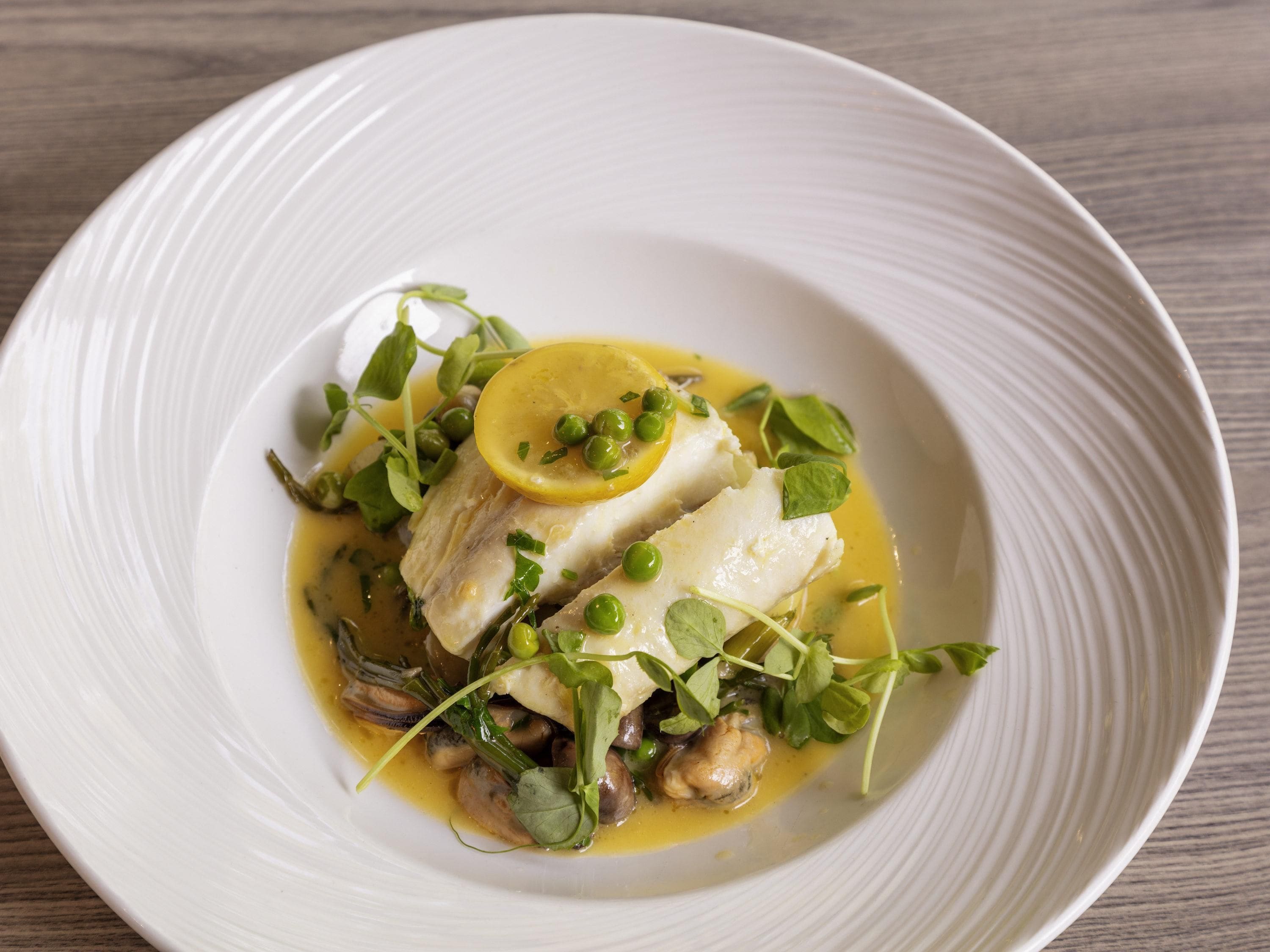 A white plate with a fish dish, garnished with green leaves and a lemon slice.