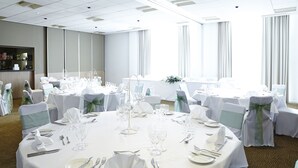 A banquet hall with round tables set for a formal event, featuring white tablecloths, glassware, and silverware.