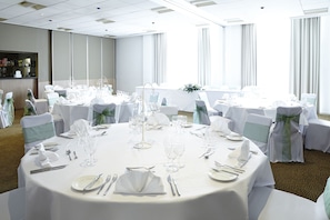 Een balzaal met ronde tafels gedekt voor een formeel evenement, met witte tafellinnen, glazen en bestek.