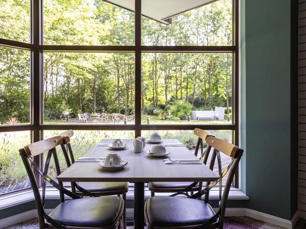 A dining area with a table set for four, large windows, and a view of the outdoors. - Novotel Newcastle Airport (Newcastle-upon-Tyne)