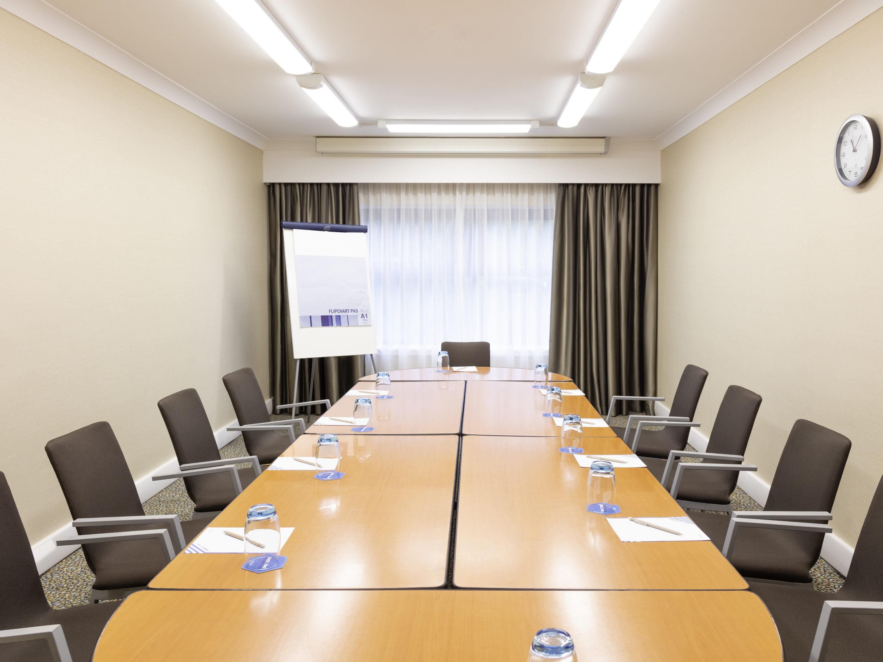 Un salón de conferencias con una larga mesa, sillas, una pizarra y un reloj en la pared.