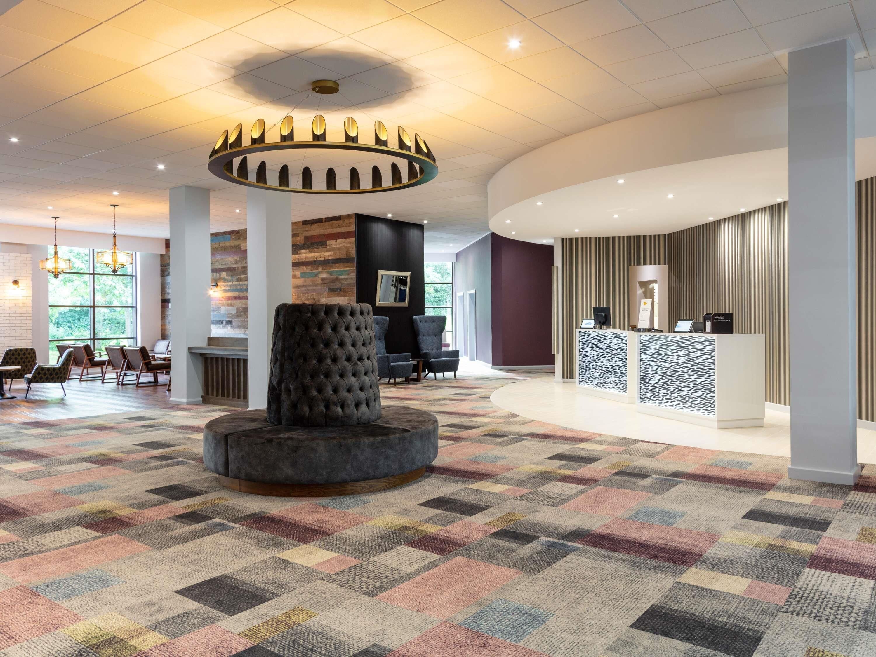 A hotel lobby with a central seating area, a reception desk, and a patterned carpet.