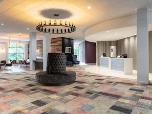 A hotel lobby with a central seating area, a reception desk, and a patterned carpet.