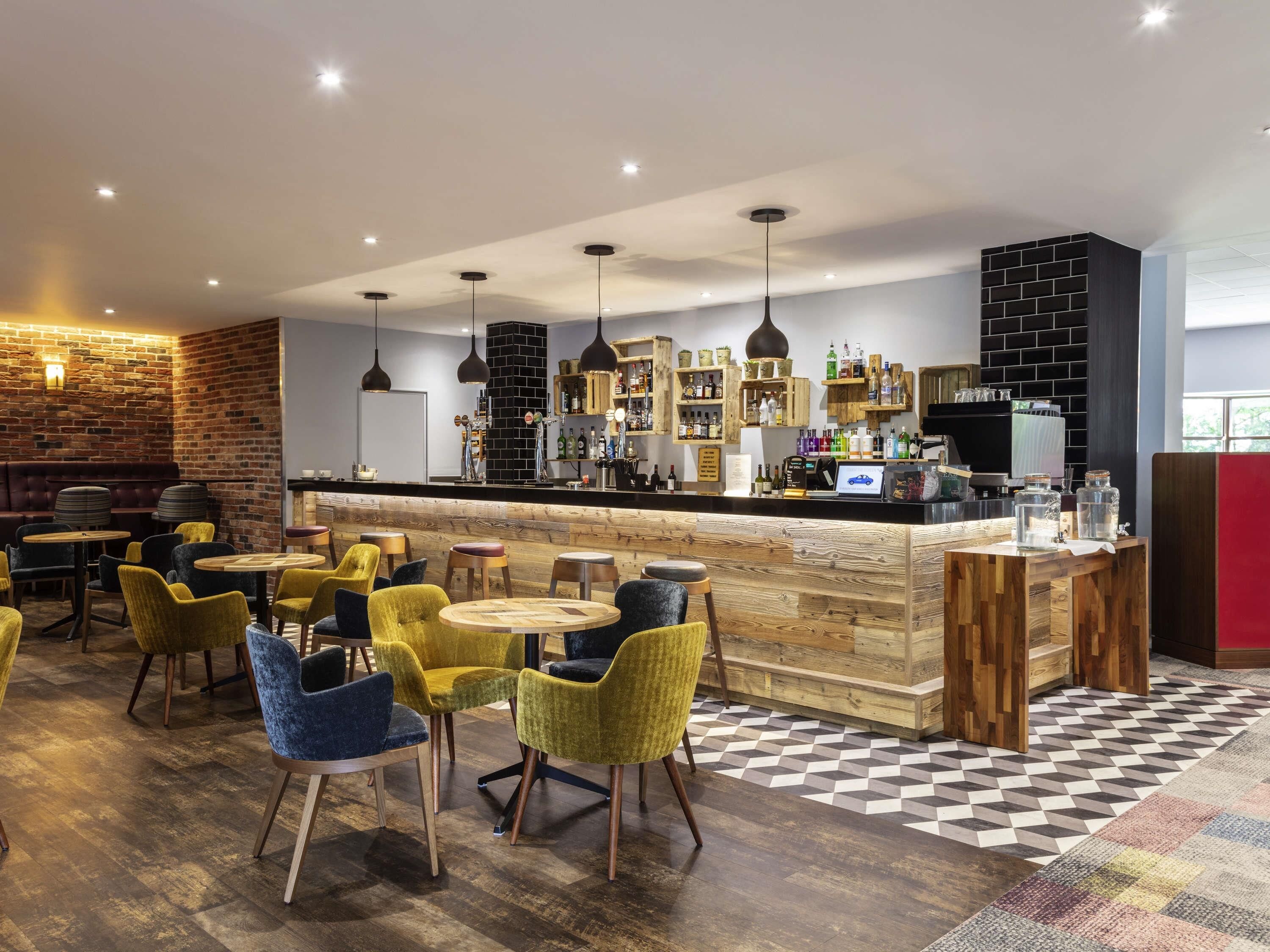 A modern bar area with wooden furniture, a checkered floor, and a brick wall.