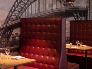 Un restaurante con asientos tapizados en rojo, una mesa de madera y una vista de un puente al fondo.