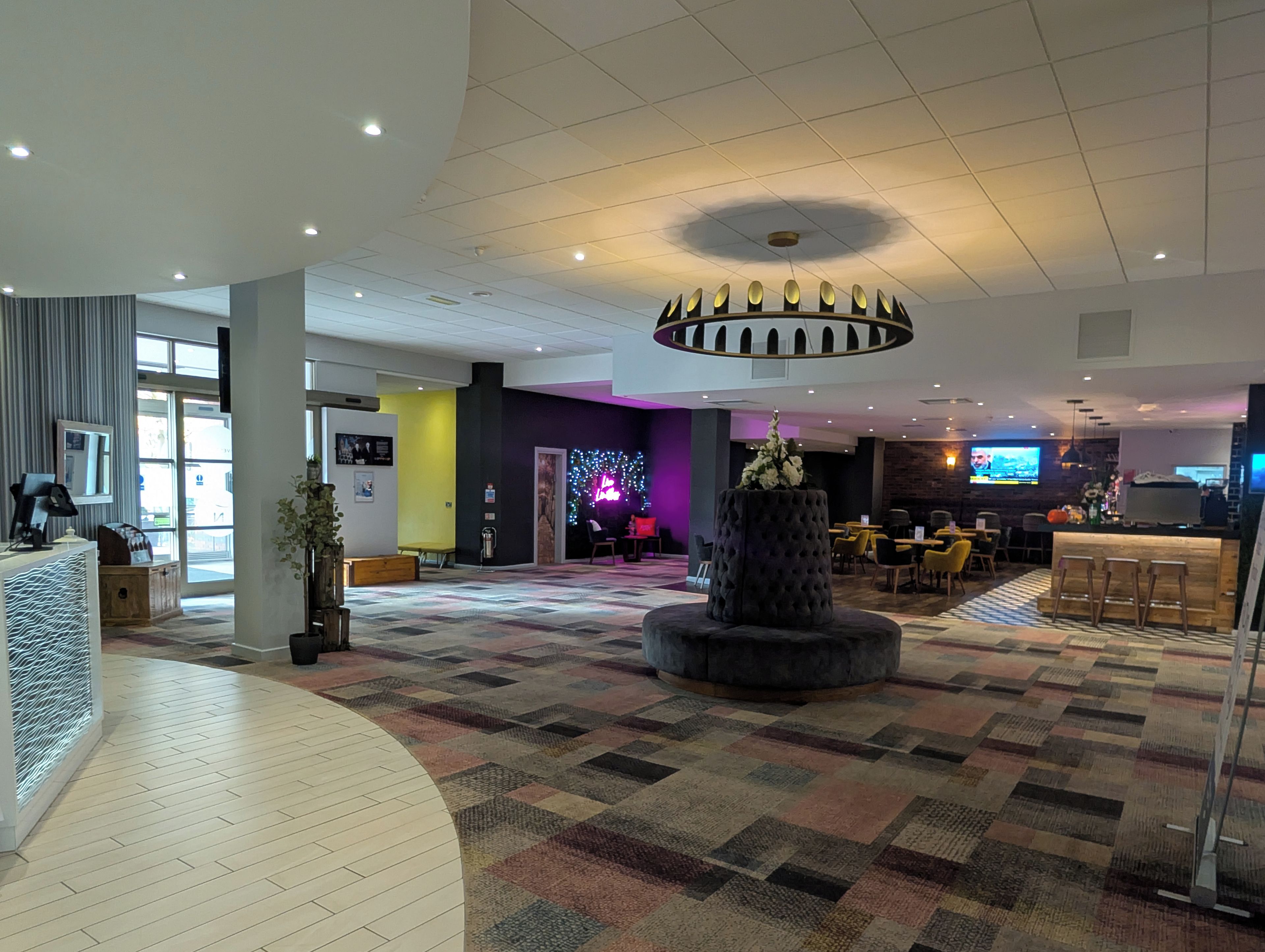 Un hall de hotel con mostrador de recepción, zona de estar y un gran macetero decorativo.