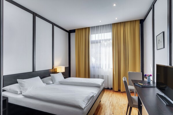 A hotel room with two beds, a desk, a chair, a lamp, and a window with curtains.