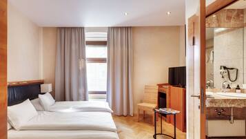 Ein Hotelzimmer mit Bett, Schreibtisch, Stuhl, Bad mit Waschbecken und Spiegel sowie einem Fenster mit Vorhängen.