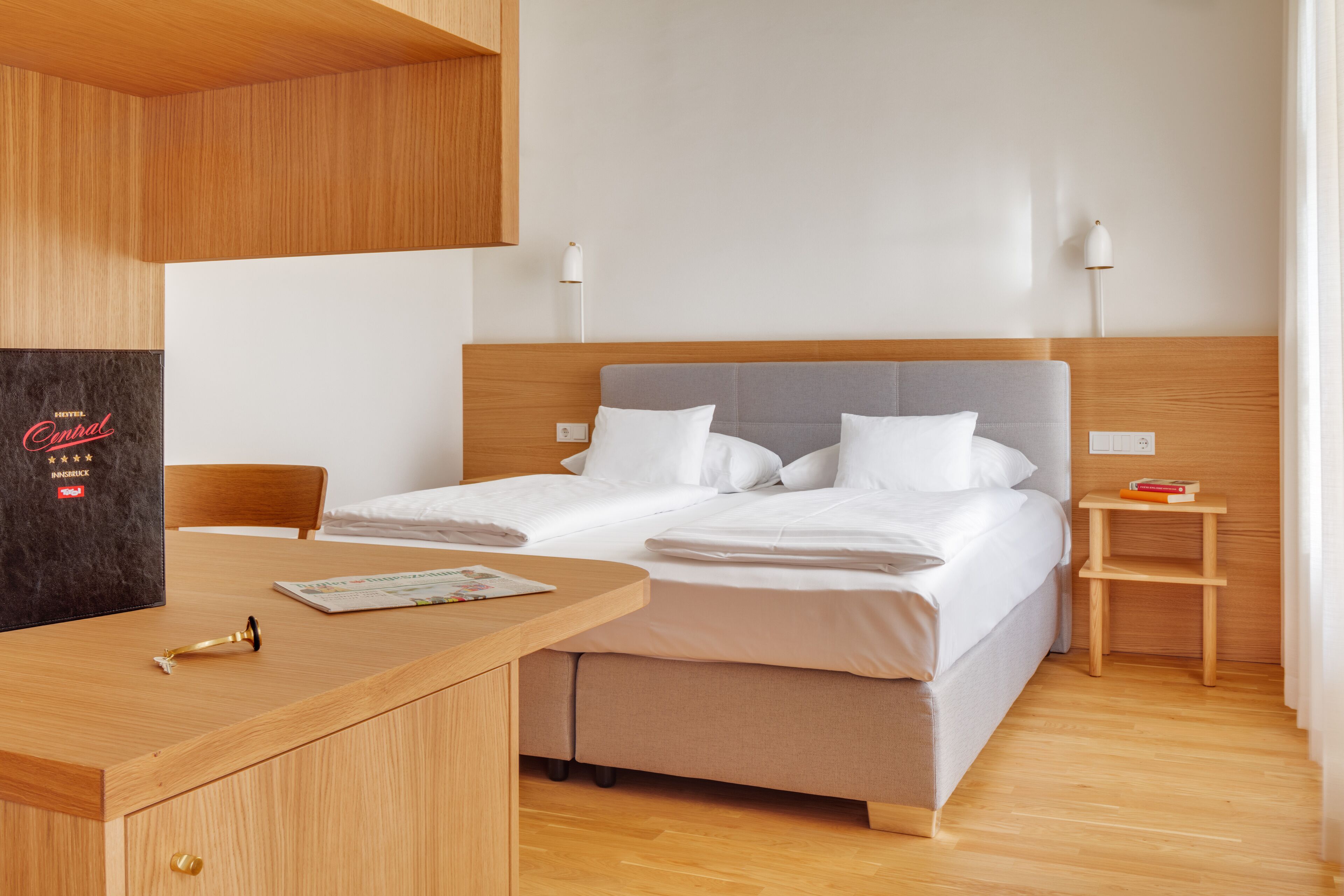 Quarto de hotel com cama, mesa de cabeceira e escrivaninha com cadeira.