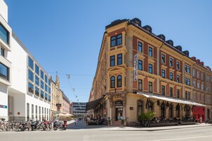 Un edificio histórico con una cafetería en la planta baja, ventanas grandes y un estilo arquitectónico clásico.