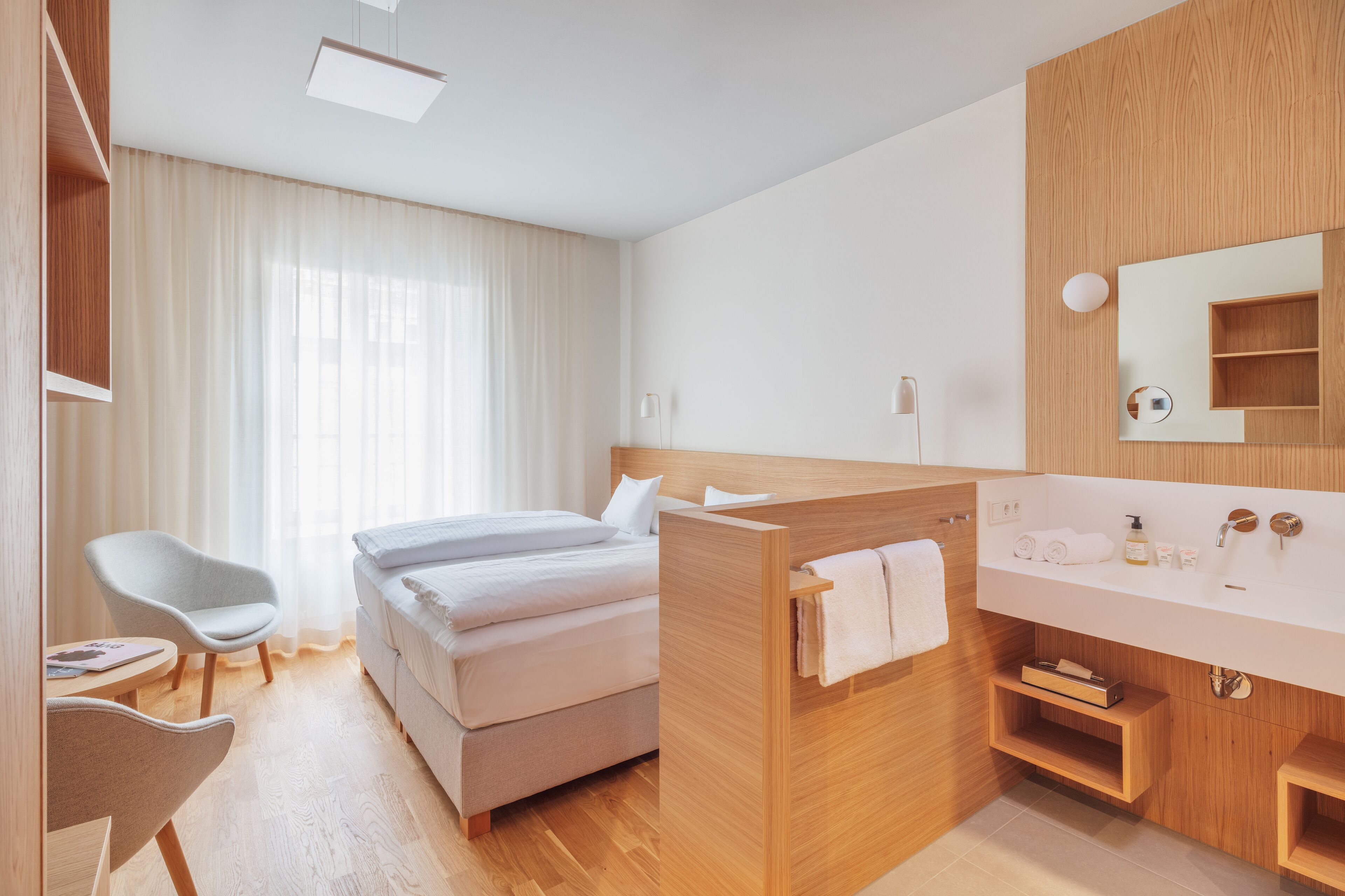 Une chambre d’hôtel moderne équipée d’un lit, d’un bureau, d’une chaise, d’une coiffeuse avec un miroir et d’un espace douche.