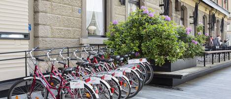A row of bicycles parked outside a building with a stone facade and large windows.