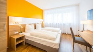 A hotel room with two beds, a wooden nightstand, a desk, and a chair. - Hotel S16 (Munich)
