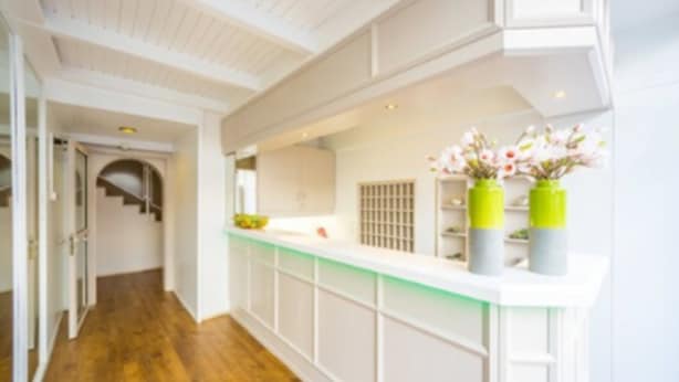 A hallway with a wooden floor, white walls, and a white reception desk with green vases. - Hotel S16 (Munich)