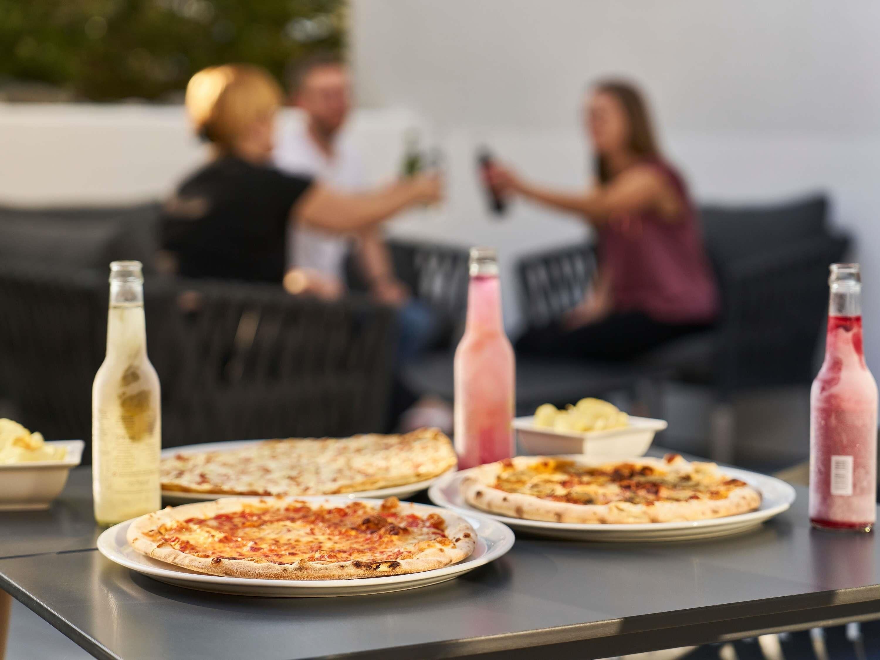 A table with pizzas and bottles of drinks, a couch, and people in the background.