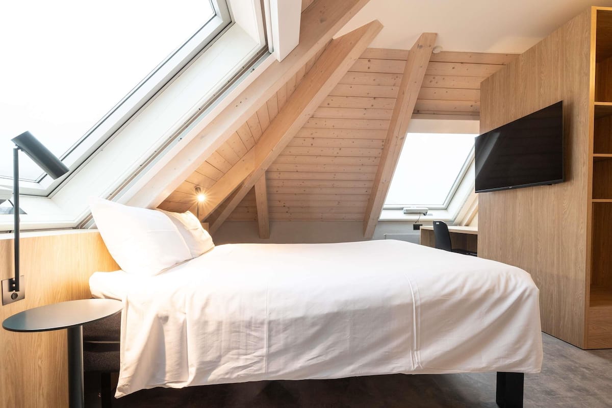 A bedroom with a skylight, a bed, a TV, and wooden walls.