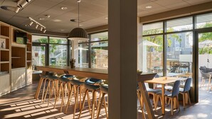 Un café moderne doté d’un bar, de coins salons et de grandes fenêtres donnant sur l’extérieur.