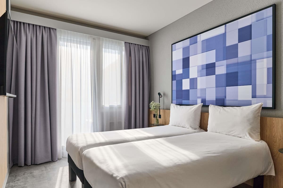 A hotel room with a large bed, a view of the city, and a modern abstract painting on the wall.