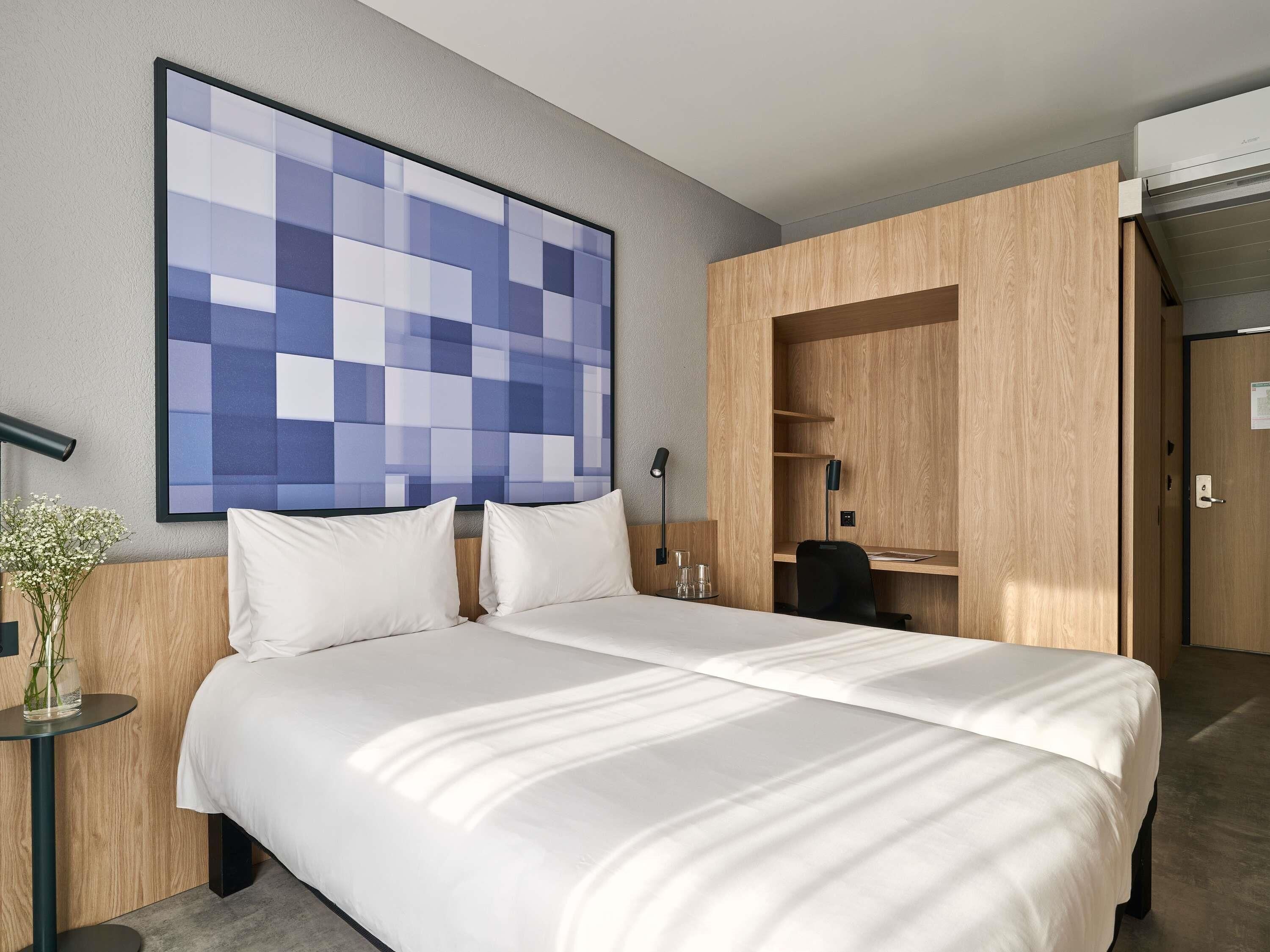 Ein Hotelzimmer mit einem großen Bett, einem Schreibtisch, einem Stuhl, einem an der Wand befestigten Fernseher und einem Holzschrank.