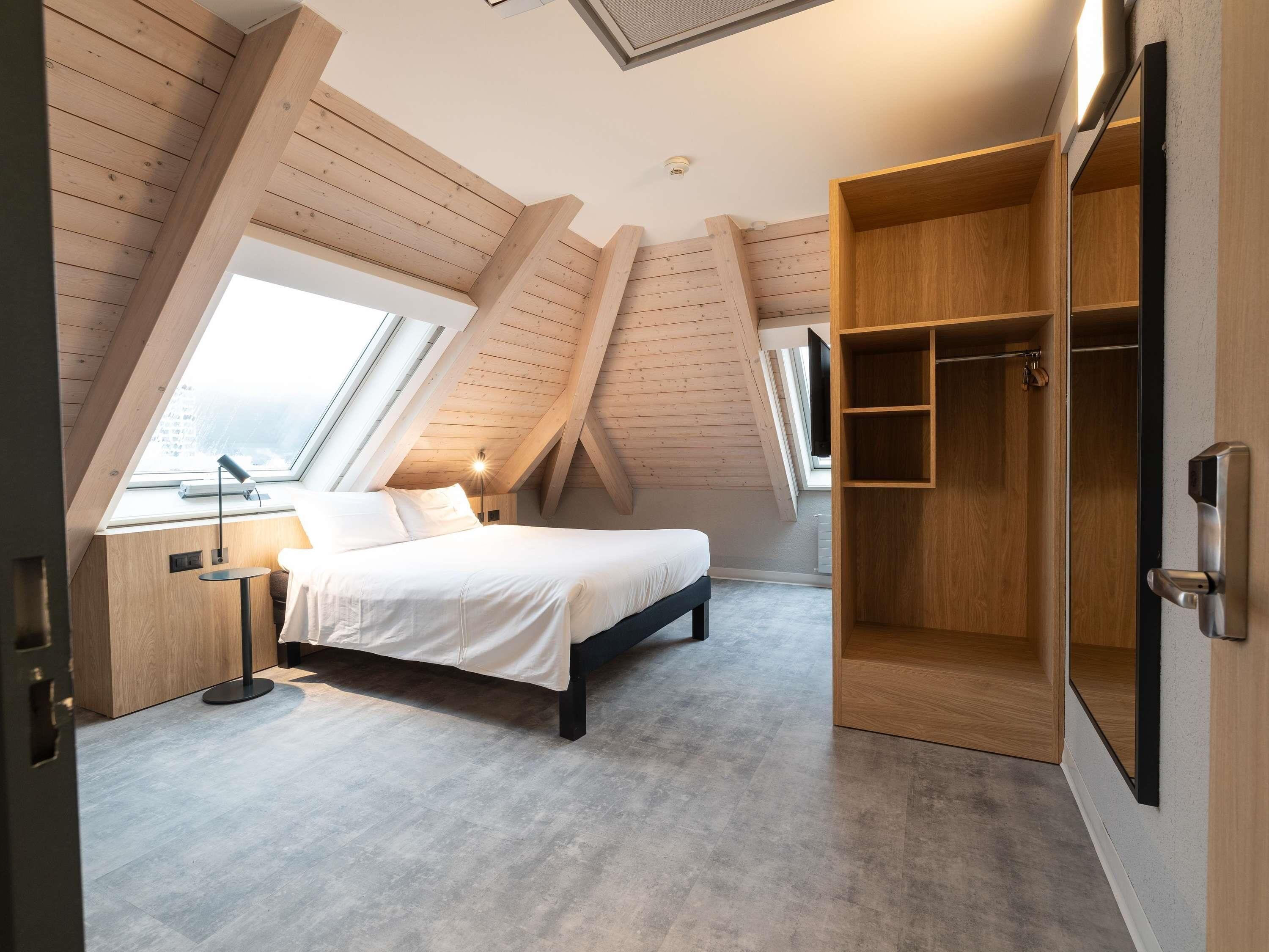 A bedroom with a sloped ceiling, a bed, a bedside table, a lamp, and a wardrobe.