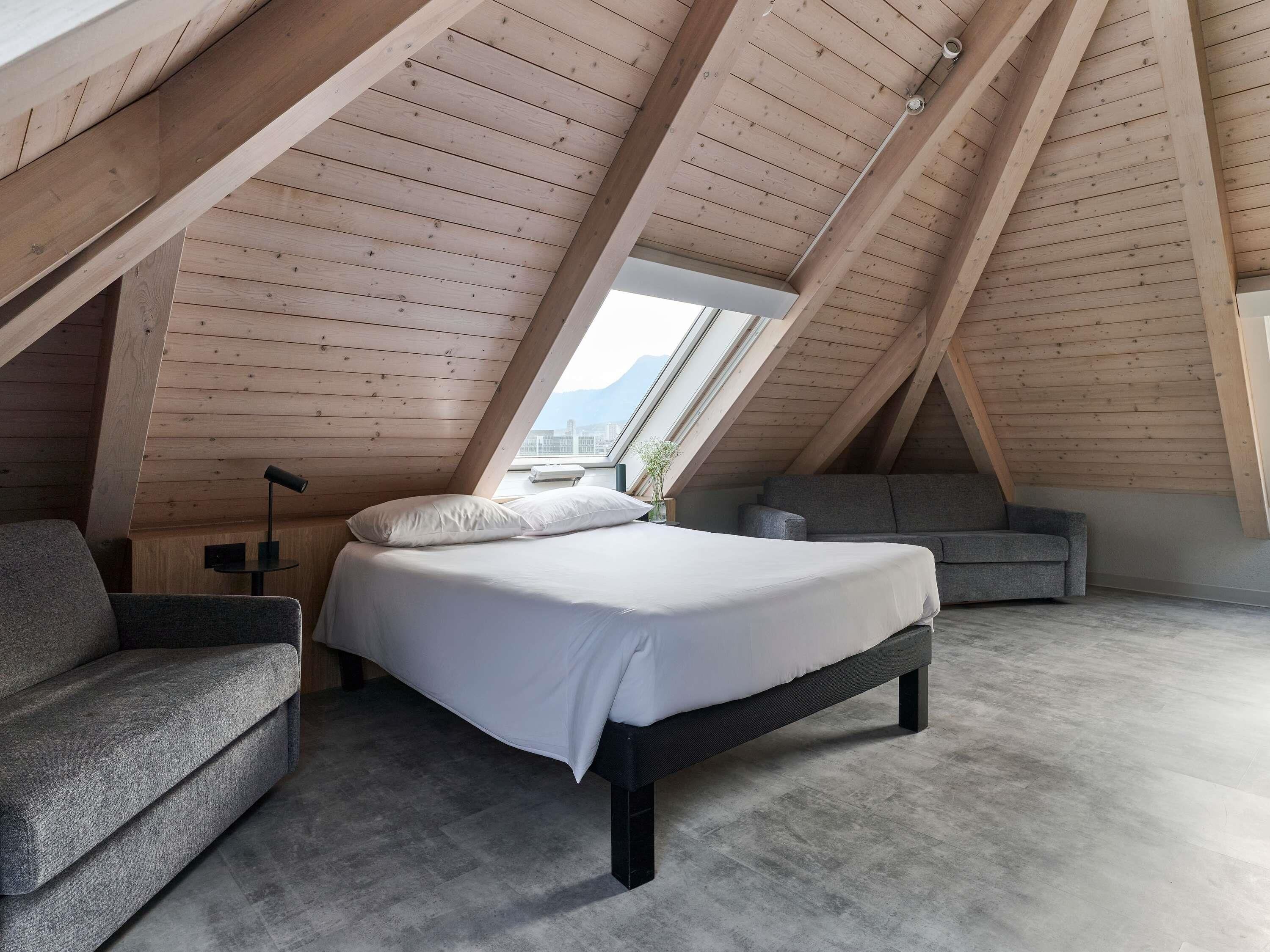Une chambre avec un plafond en pente, un lit, un canapé et une vue sur le ciel grâce à une lucarne.