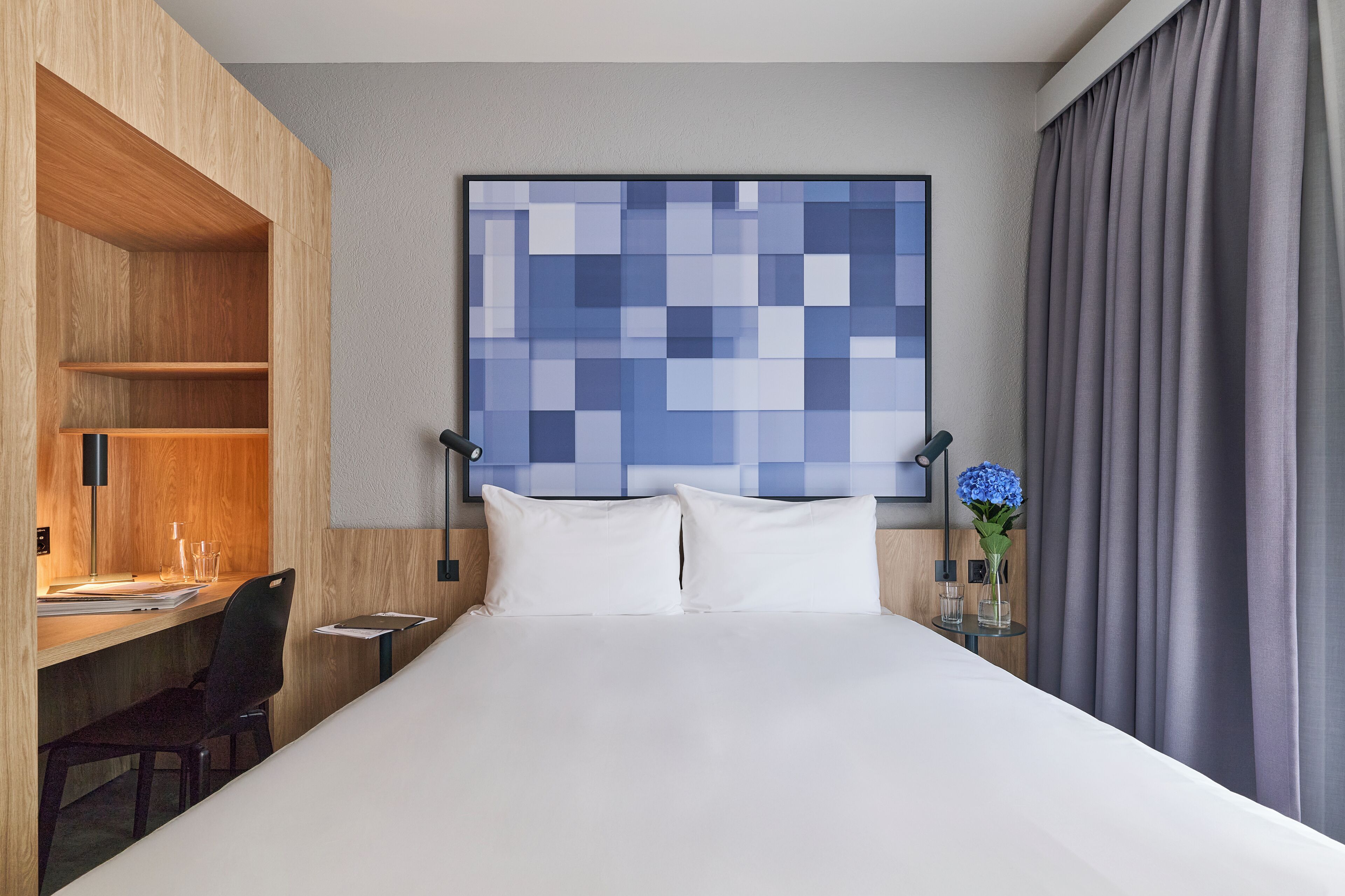 A hotel room with a bed, a desk, a chair, a nightstand, and a wall art piece.