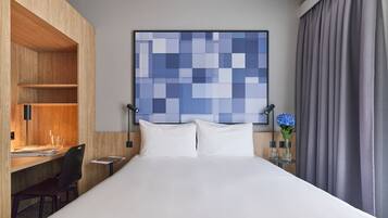 A hotel room with a bed, a desk, a chair, a nightstand, and a wall art piece.