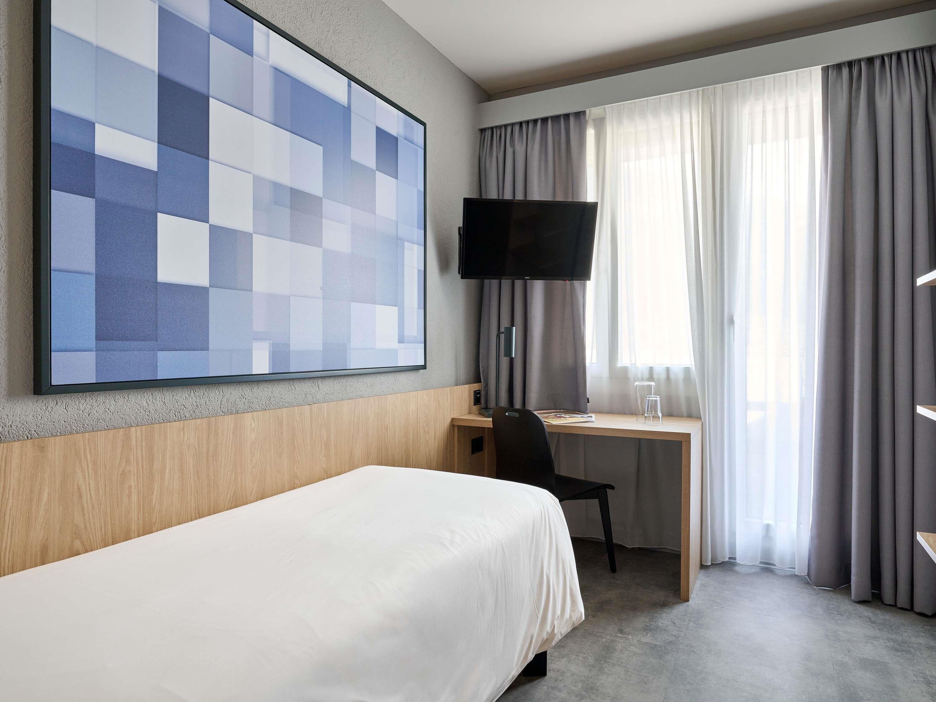 Une chambre d’hôtel avec un lit, un bureau, une chaise, une télévision et une fenêtre avec des rideaux.