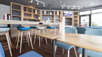 Ein modernes Café-Interieur mit Holztischen und blauen Stühlen, einer Theke mit Speisekarte und einem großen Fenster, das für natürliches Licht sorgt.