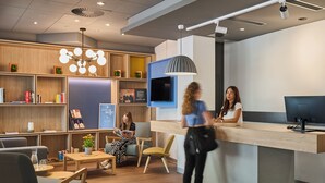 Un espace d’accueil moderne, doté d’un comptoir de réception en bois, de sièges confortables et d’un grand luminaire suspendu.