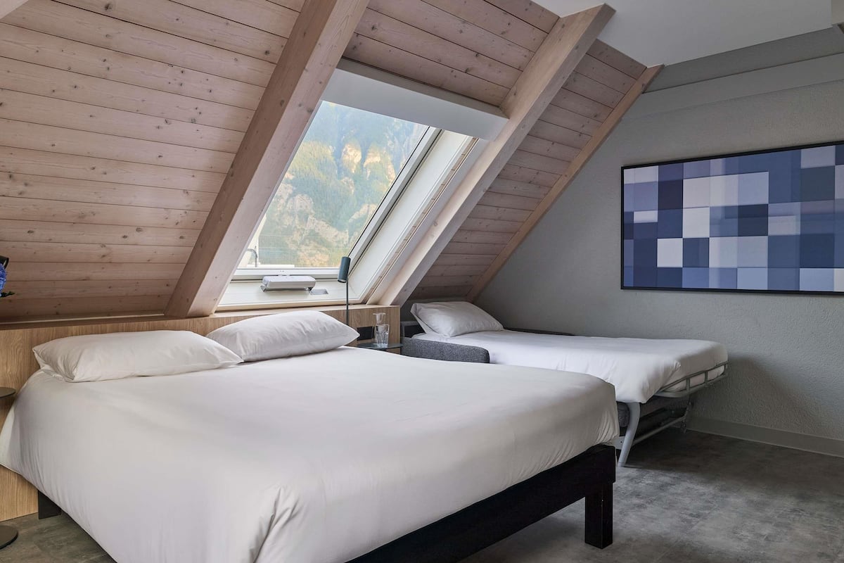 A bedroom with two beds, a skylight, a view of mountains, and a blue abstract painting on the wall.
