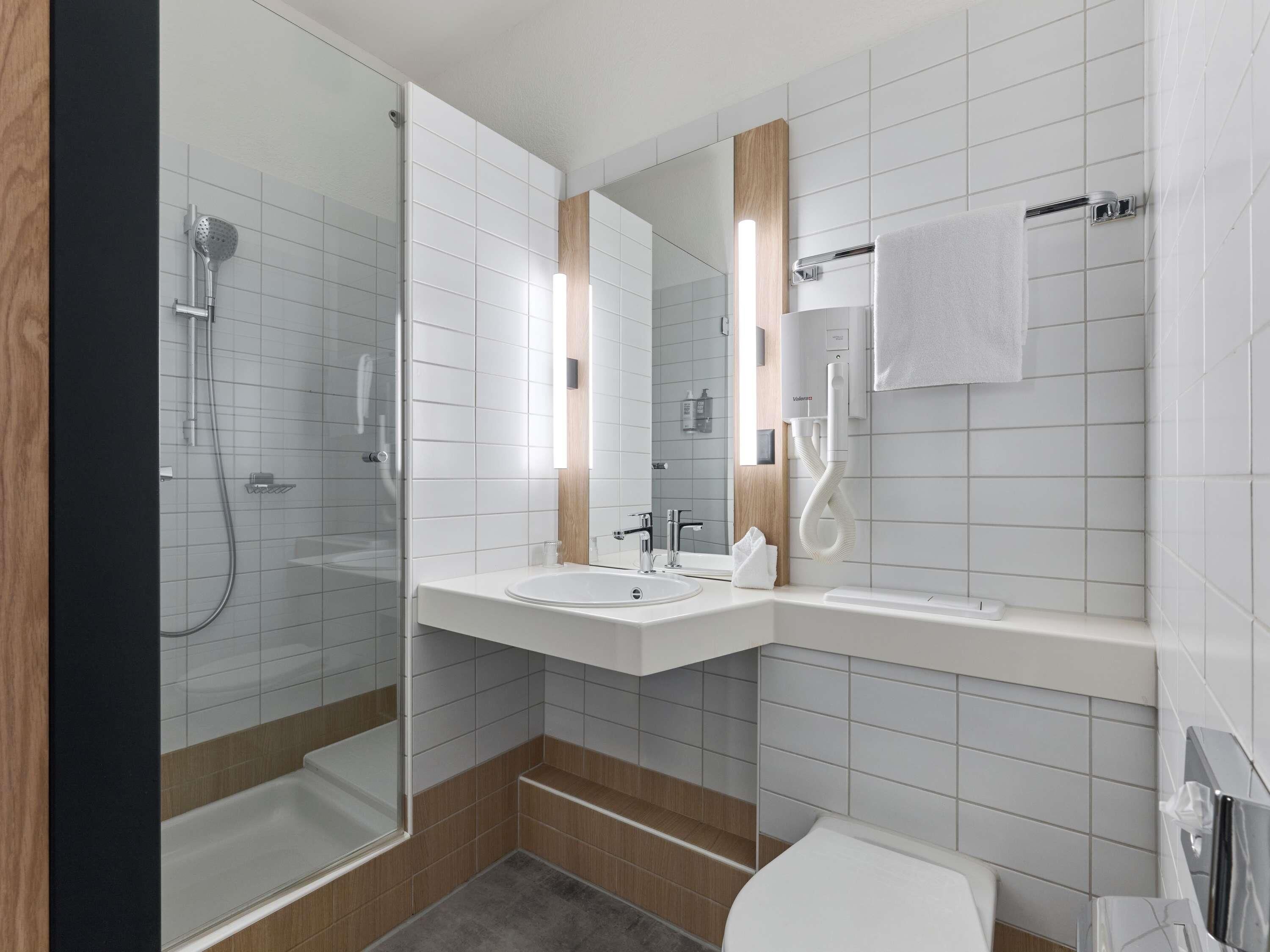 A modern bathroom with a glass-enclosed shower, two sinks, a toilet, and a towel rack.