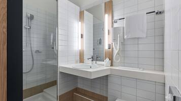A modern bathroom with a glass-enclosed shower, two sinks, a toilet, and a towel rack.