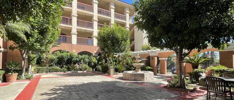 A courtyard with a fountain, potted plants, and a building with balconies.