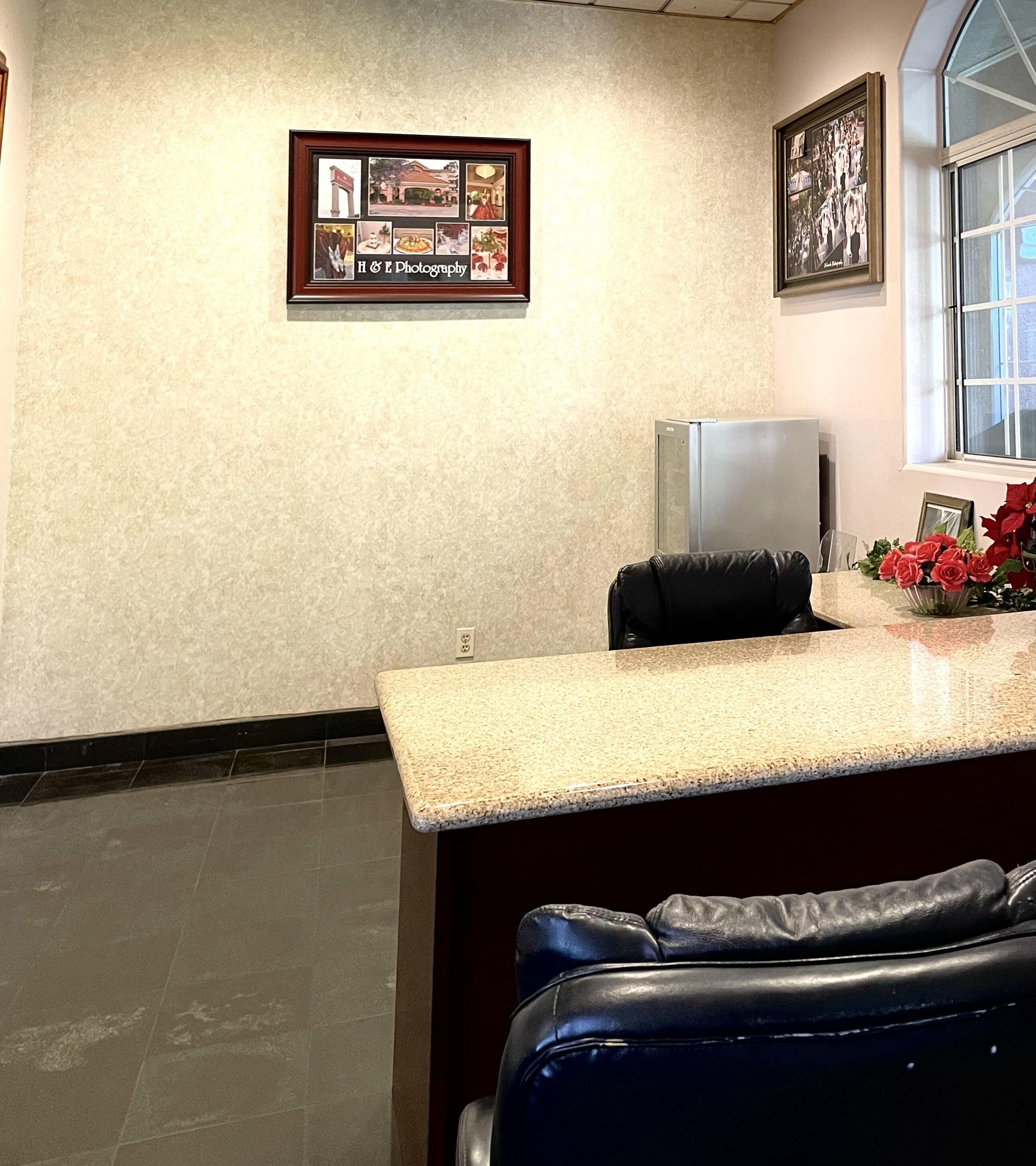 A reception area with a counter, a refrigerator, a framed photo collage, and a window with a view.