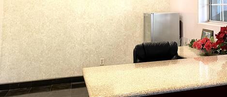 A reception area with a counter, a refrigerator, a framed photo collage, and a window with a view.